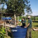 Fotografia de aluna da UFGD junto a um homem do assentamento, eles estão verificando o tanque de peixes que faz parte do sistema de aquaponia