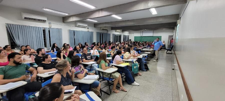 Na foto pode-se ver um auditório com mais de 60 pessoas no público e um professor em frente a essas pessoas. 