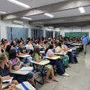 Na foto pode-se ver um auditório com mais de 60 pessoas no público e um professor em frente a essas pessoas. 