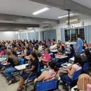 Na foto pode-se ver um auditório com mais de 60 pessoas no público e um professor em frente a essas pessoas. 