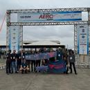 A foto ontém 15 jovens que estão posando em frente a um pórtico onde está escrito SAE Brasil AeroDesign