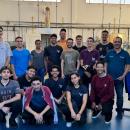 Na foto 16 pessoas, a maioria jovens estudantes, estão posando em um laboratório de física, onde tem dois computadores e outros equipamentos. 